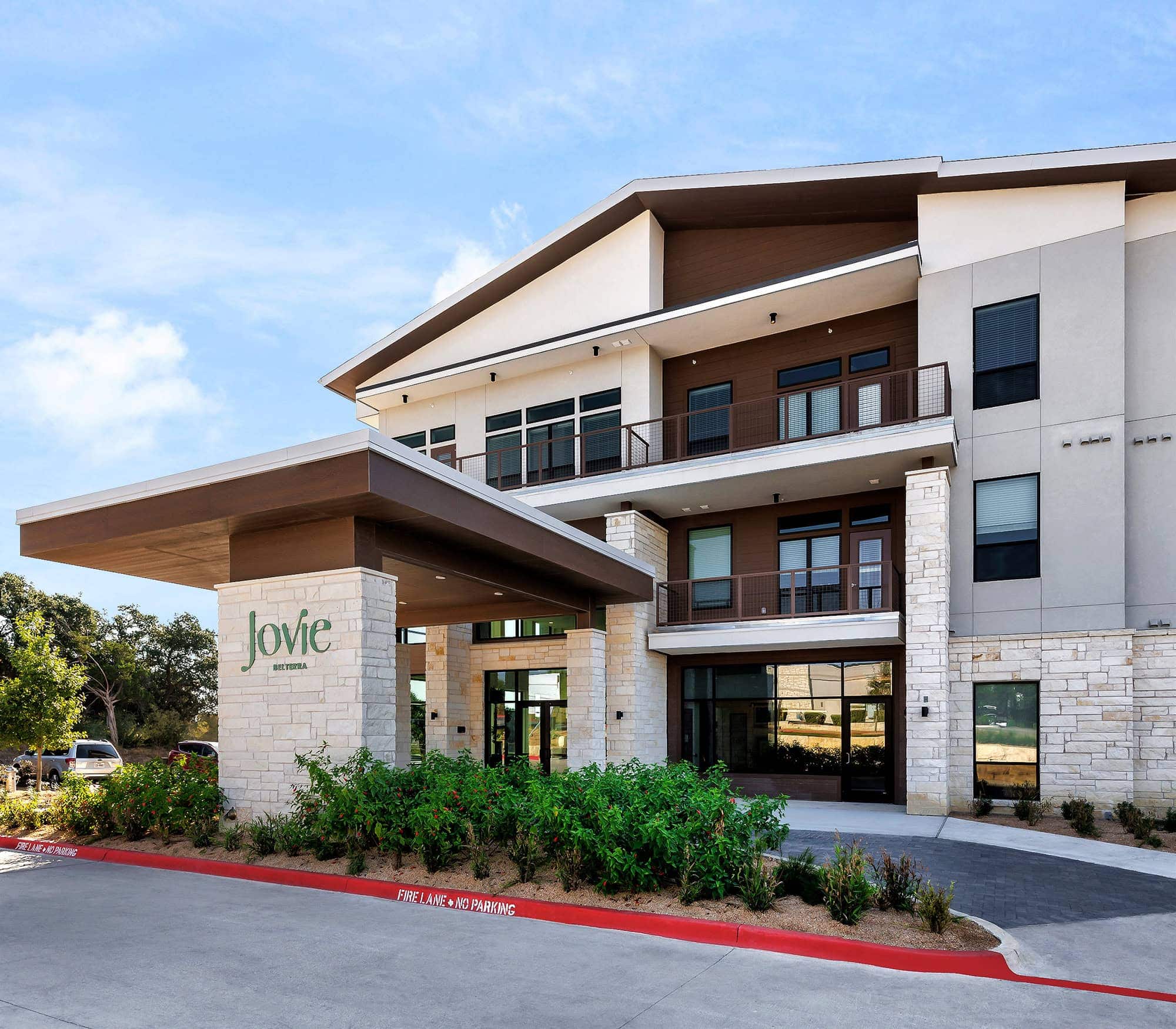 The exterior of the Jovie Belterra senior living community in Austin, TX, featuring parking spots and balconies.