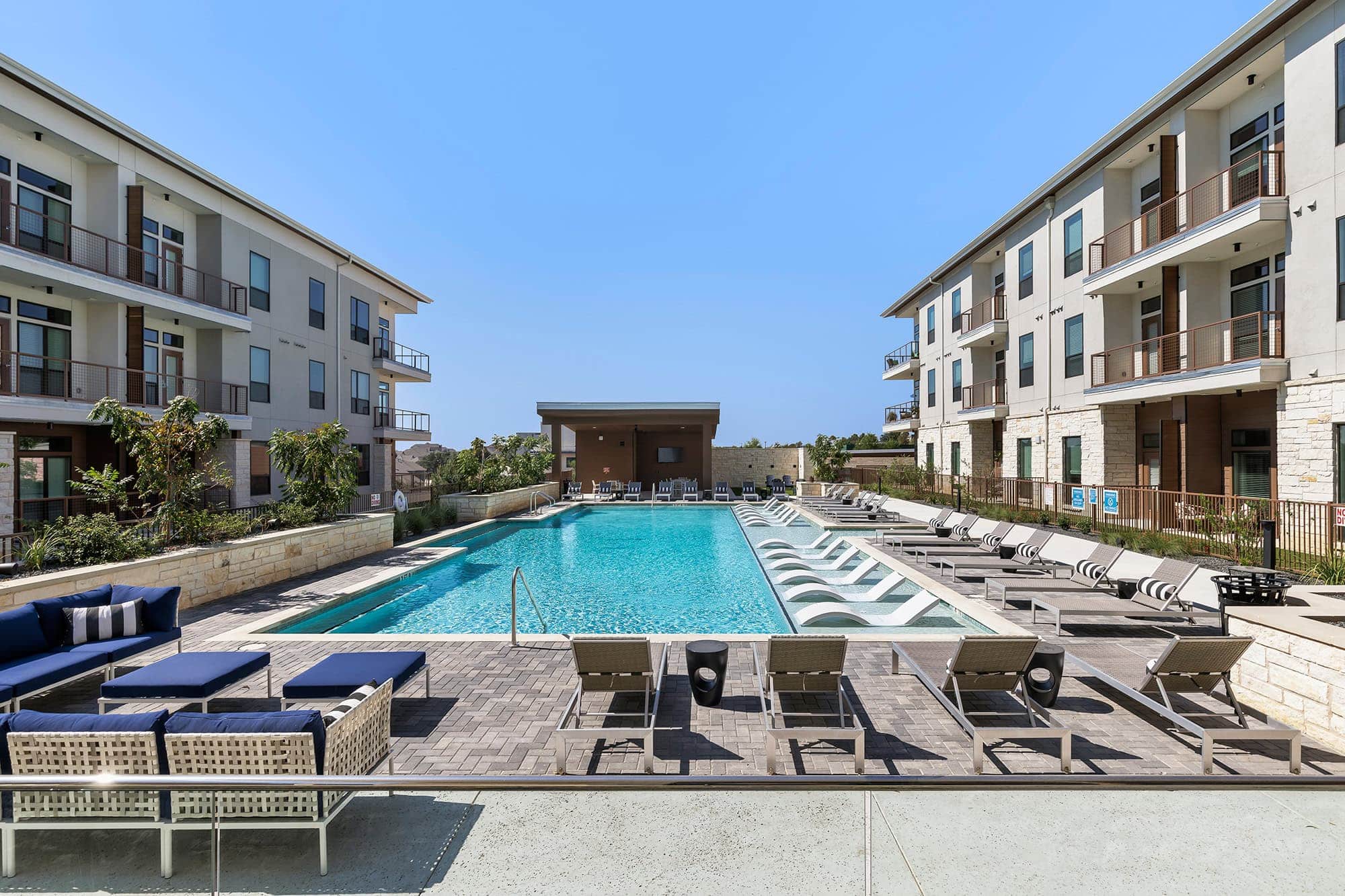 The pool area at our 55 and over community in Austin, TX, featuring a shade structure and view of the apartments.