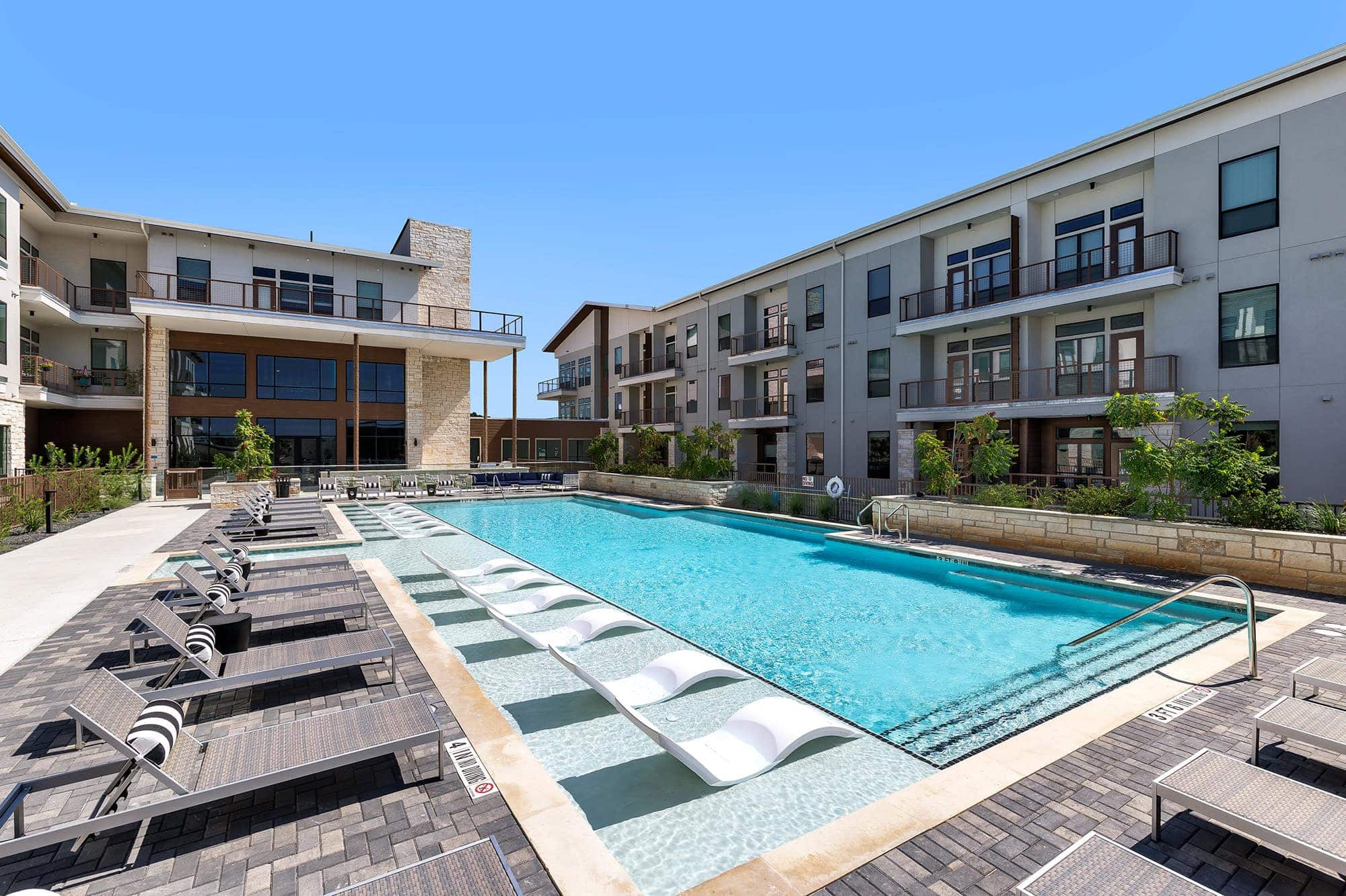 The pool area at our 55 and over community in Austin, TX, featuring a shade structure and view of the apartments.